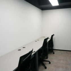 Bright internal three-person office suite with white desks and black chairs.
