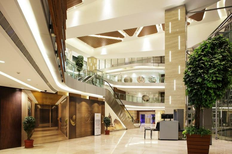 Grand multi-level lobby of The Capital building with warm lighting, indoor trees, and modern architectural details.