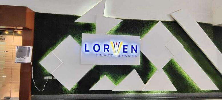 Reception area at Vaishnavi Cynosure featuring a modern branded wall with geometric panels and green accents.