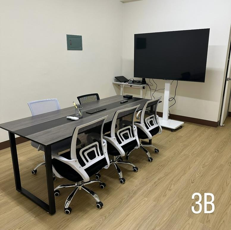 Modern conference room with a dark wood table, several white mesh chairs, and a large flat-screen TV.