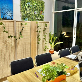 Communal workspace with a long wooden table, laptops, and a lush green feature wall near the window.. Click for details.