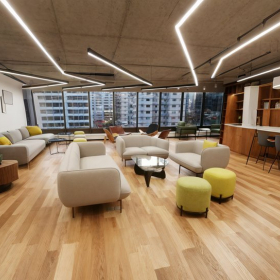 Modern open-plan lounge with stylish grey sofas, yellow ottomans, and wood flooring.. Click for details.